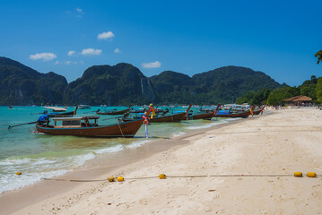 A tranquil beach on Koh Phi Phi, Thailand, with long tail boats adorned with ribbons, turquoise...