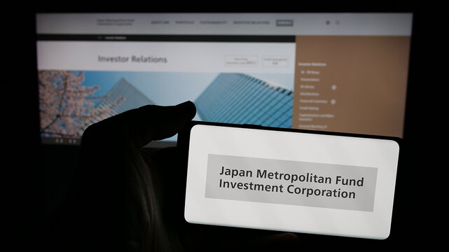 Stuttgart, Germany - 01-14-2025: Person holding mobile phone with logo of Japan Metropolitan Fund Investment Corporation (JMF) on screen in front of web page. Focus on phone display.