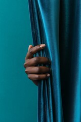 Obraz premium Dark Brown Hand Pulling Teal Velvet Curtain in Dramatic Lighting