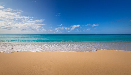 A sand beach with a stunning turquoise sea and a bright blue sky dotted with fluffy white clouds.