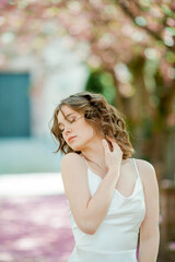 Portrait of young woman near blooming sakura tree in European city.