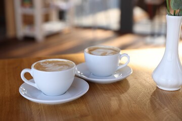 Cups of aromatic coffee on wooden table in cafe, closeup