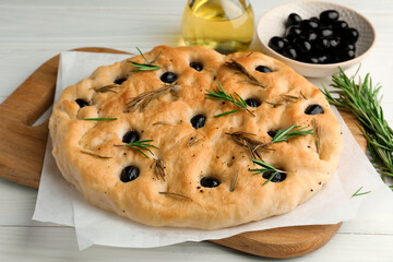 Delicious focaccia bread with olives, rosemary and oil on white wooden table, closeup
