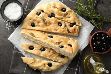Slices of delicious focaccia bread with olives, rosemary, oil and salt on grey table, flat lay