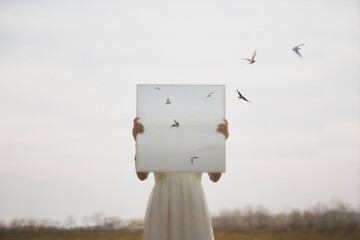 woman with canvas in front of her face from which birds fly in a field