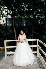 bride in a wedding dress. She is standing on the porch of a wooden house. The dress is white,...