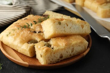 Slices of delicious focaccia bread with olives, thyme and salt on black table, closeup