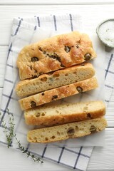 Slices of delicious focaccia bread with olives, thyme and salt on white wooden table, flat lay