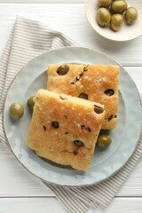 Slices of delicious focaccia bread with olives, thyme and salt on white wooden table, flat lay