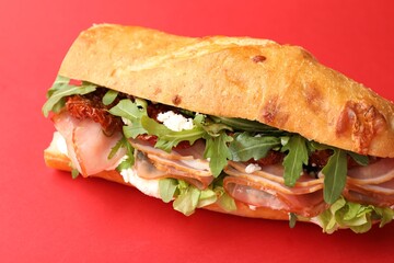 Baguette sandwich with ham and sun dried tomatoes on red background, closeup