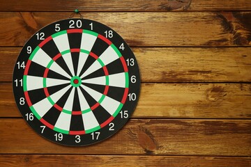 Dart board hanging on wooden background, space for text