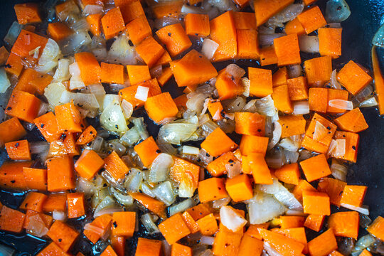 Diced carrots and onions are fried in a pan. Background with the texture of roasted vegetables.