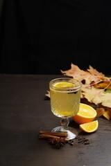 White mulled wine in a transparent glass on a dark table among fruits and spices