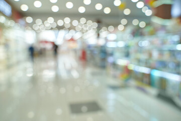 Blurred view of busy shopping mall with bright lights and shoppers in motion.