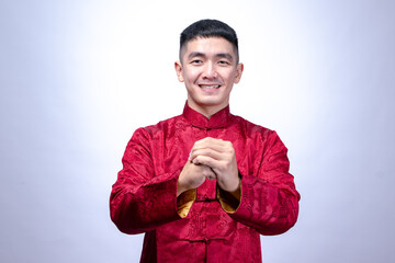 A smiling young man in a red traditional Chinese Tang suit performs a Gong Xi greeting gesture,...