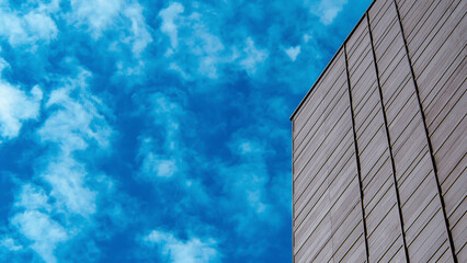 Minimalistic shot of a modern building facade with a vibrant blue sky and scattered clouds, ideal for architectural themes, urban designs, or as a sky backdrop