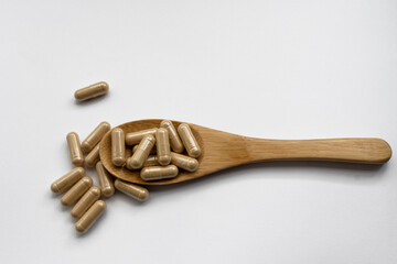 Herb capsule, Nutritional Supplement pill on a wooden spoon isolated on white