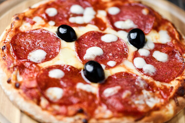 Pizza with salami and mozzarella cheese. Wooden background. Soft focus. Close up.