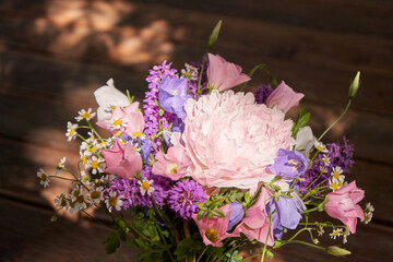 Vibrant bouquet of pink peony, purple flowers, and white daisies in sunlit setting.