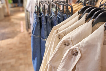 Naklejka premium Casual denim jeans and beige coats on hangers in clothing store display.
