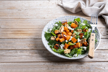 Pumpkin salad with arugula, walnuts and feta cheese on wooden. Copy space