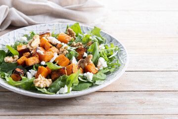 Pumpkin salad with arugula, walnuts and feta cheese on wooden. Copy space