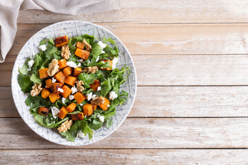 Pumpkin salad with arugula, walnuts and feta cheese on wooden. Top view. Copy space