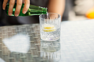 Man's hand pouring sparkling water into a glass with lemon close-up