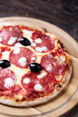 Pizza with salami and mozzarella cheese. Wooden background. Soft focus. Close up.