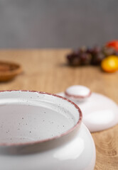 White ceramic clay pot with lid for roasting meat and vegetables stands on kitchen wooden table