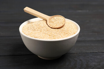 Oat bran in bowl and spoon on black wooden table, closeup