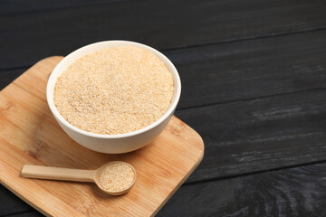 Oat bran in bowl and spoon on black wooden table, space for text