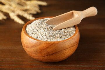 Fresh rye bran in bowl and scoop on wooden table, closeup