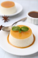 Tasty pudding with caramel sauce served on white tiled table, closeup