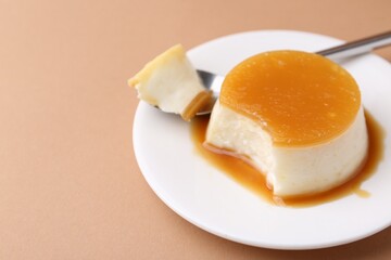 Fototapeta premium Tasty pudding with caramel sauce served on light brown background, closeup. Space for text