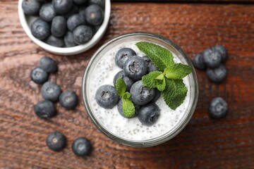 Delicious chia pudding with blueberries and mint in glass on wooden table, flat lay