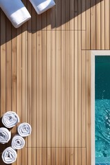 Wooden floor near the pool with natural and warm wood tone. Part of the clean sparkling pool with turquoise water is visible. Several neatly folded white towels are lying on the floor