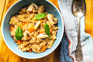 Boiled spelled or spelled porridge with mushrooms, carrots and spinach in a blue bowl on a wooden background with a napkin and spoon. Healthy eating concept. Vegetarian dish.