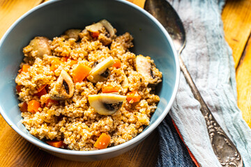 Boiled spelled or spelled porridge with mushrooms, carrots and spinach in a blue bowl on a wooden background with a napkin and spoon. Healthy eating concept. Vegetarian dish.