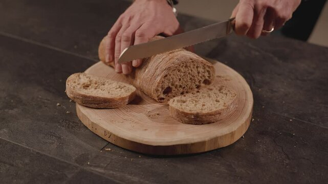 A close-up of hands slicing a crusty loaf of artisanal bread on a rustic wooden cutting board, capturing the natural texture and simplicity of homemade food preparation. Slow motion