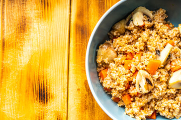 Boiled spelled or spelled porridge with mushrooms, carrots and spinach in a blue bowl on a wooden background with a napkin and spoon. Healthy eating concept. Vegetarian dish. Copyspace