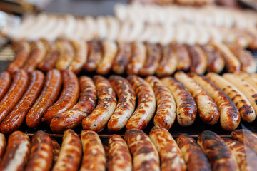 Close-up of assortment juicy bratwurst sausages and meat steaks cooking on grill at German street...