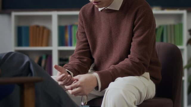 Tilt down slowmo of introverted Asian teenage boy opening up about difficulties and feeling vulnerable during individual therapy consultation with unrecognizable school counselor