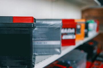 Close-up of a black car battery with a red terminal, placed on a store shelf. Blurred background features a variety of colorful batteries on display. Ideal for automotive and energy-related concepts