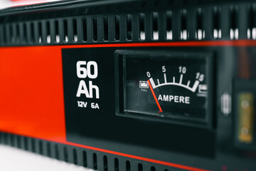 Close-up view of a battery charger with an ampere gauge and capacity indicator displaying 60 Ah. The red needle points to full charge on a black and red device