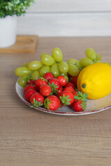Plate with fresh strawberries, grapes and lemon on the table