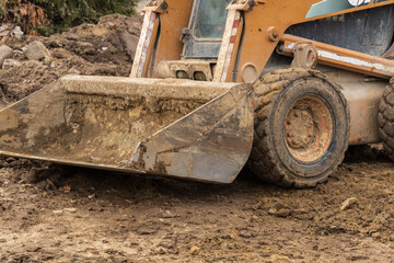 Heavy machinery, including a backhoe, is actively digging and transporting soil at a construction site surrounded by dirt and debris