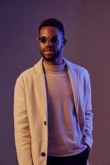 Obraz premium Stylish young man wearing sunglasses and modern attire poses confidently against a vibrant backdrop, showcasing contemporary fashion trends and emotions