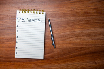 Notepad with text 2025 Priorities, on wooden surface. Priorities and goals for 2025