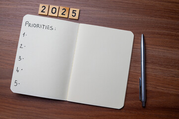 Notepad with text 2025 Priorities, on wooden surface. Priorities and goals for 2025